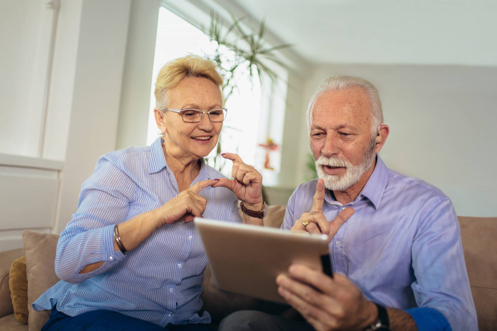 Smiling deaf senior couple talking using sign language on the digital tablet’s cam