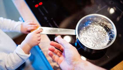 Image of a child's hand next to a boiling pot of water on a stove.