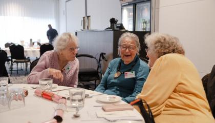 An image of Doreen Cavanaugh with two other ladies, enjoying a Christmas lunch at a fully setup dinner table.