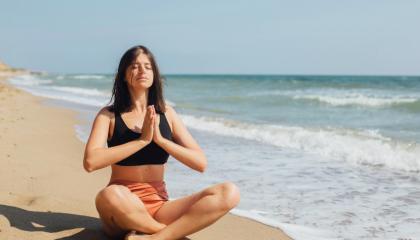 An image of a woman sat on the shoreline meditating.