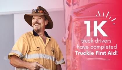 An image of a truck driver smiling to the camera, dressed in high vis and a wide brimmed hat. Sidelined by the text '1K truck drivers have completed Truckie First Aid!'.