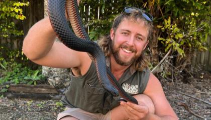 An image of Mick from Wildlife Unleashed holding a snake outdoors.