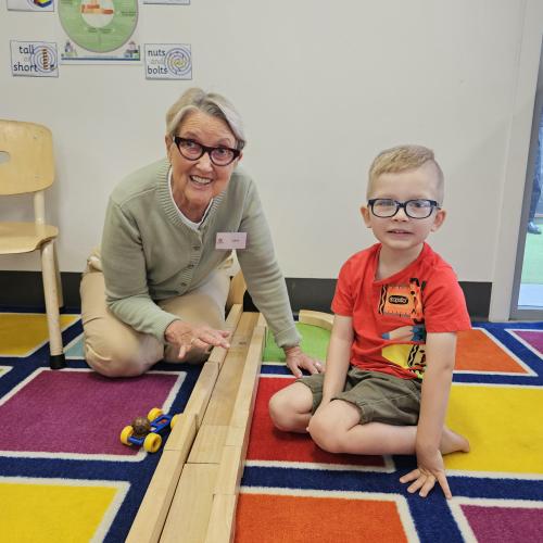 An image of an older lady playing with a young boy on a colourful playmat