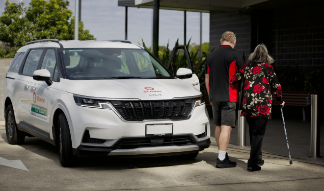 An image of a staff member and a client walking past a St John vehicle.