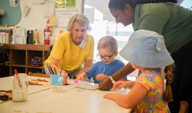 An image of two children doing craft with an older woman and an educator.