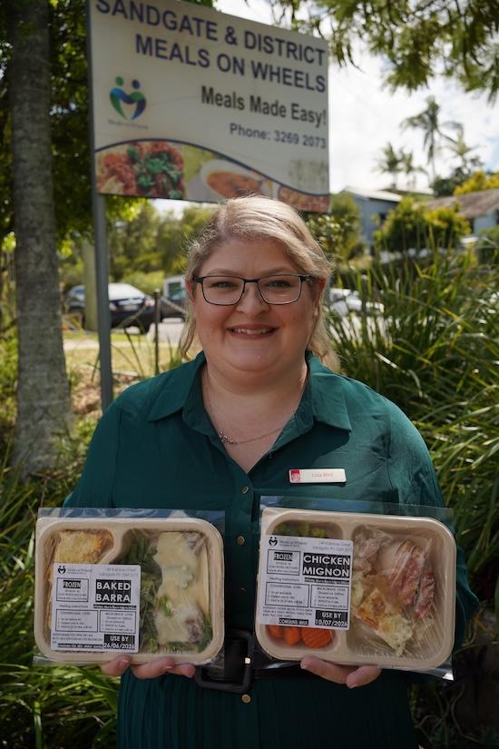 An image of a St Johns volunteer smiling while holding two meals provided by Meals on Wheels