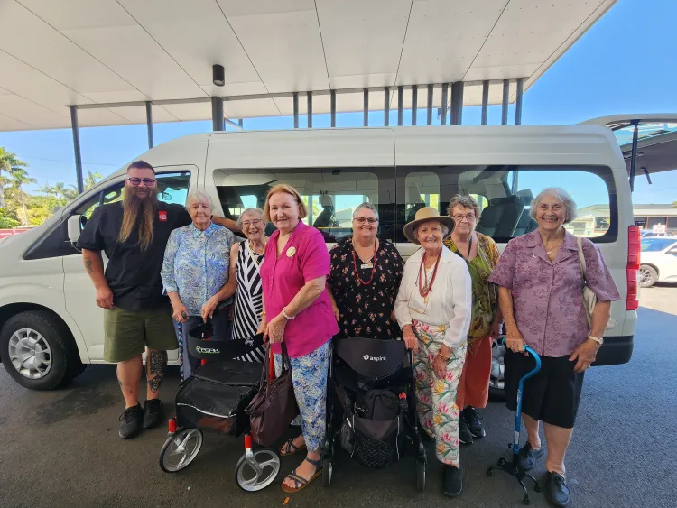 An image of a social group stood together outside of a community van, smiling.