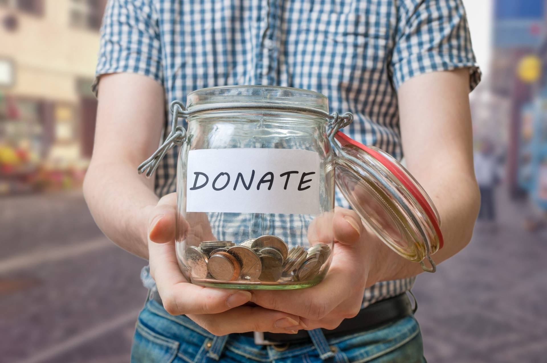 Man standing on street is collecting donations in jar.