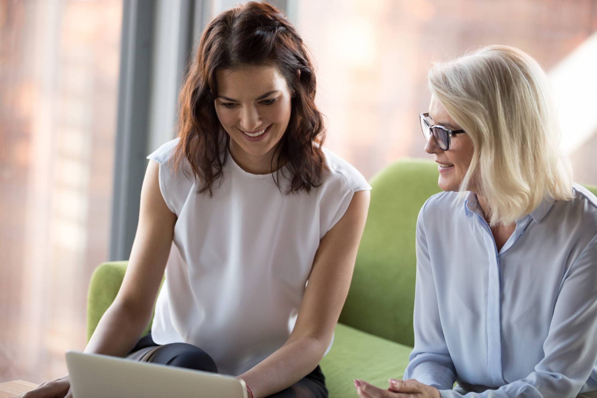 Senior and young colleagues women sitting looking at laptop screen