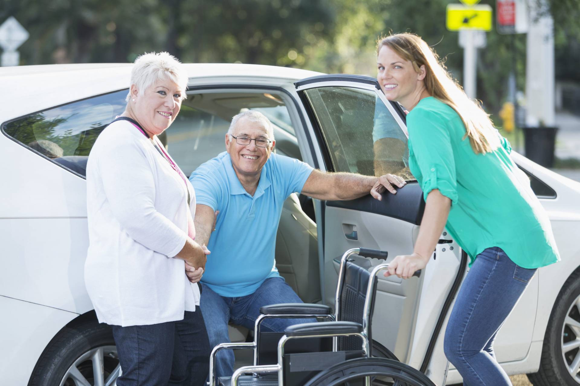 Family helping senior man from car to wheelchair